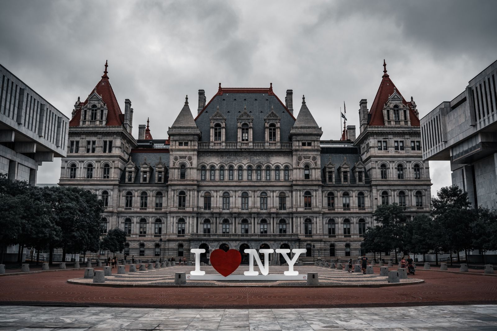 The New York State Capitol in Albany under gray clouds, with a large I Love NY sign on the plaza in front